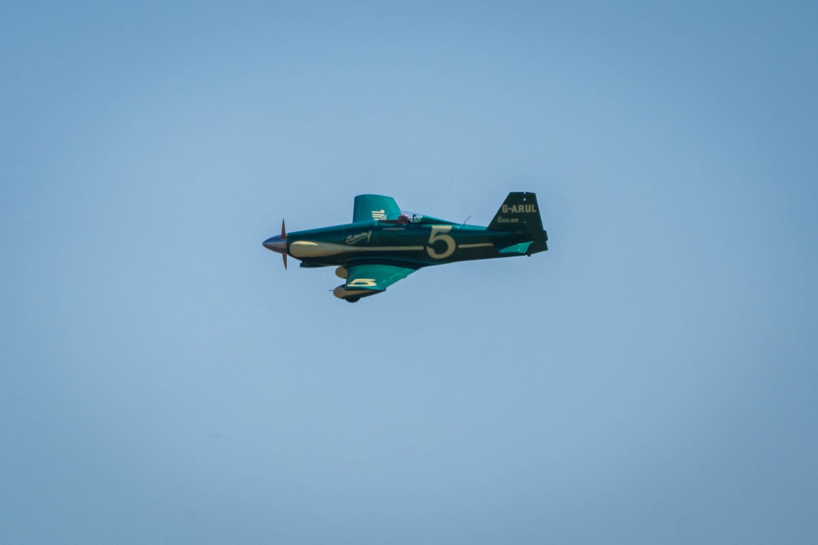 The green and cream LeVier Cosmic Wind G-ARUL, race number 5, in flight against a pale sky.