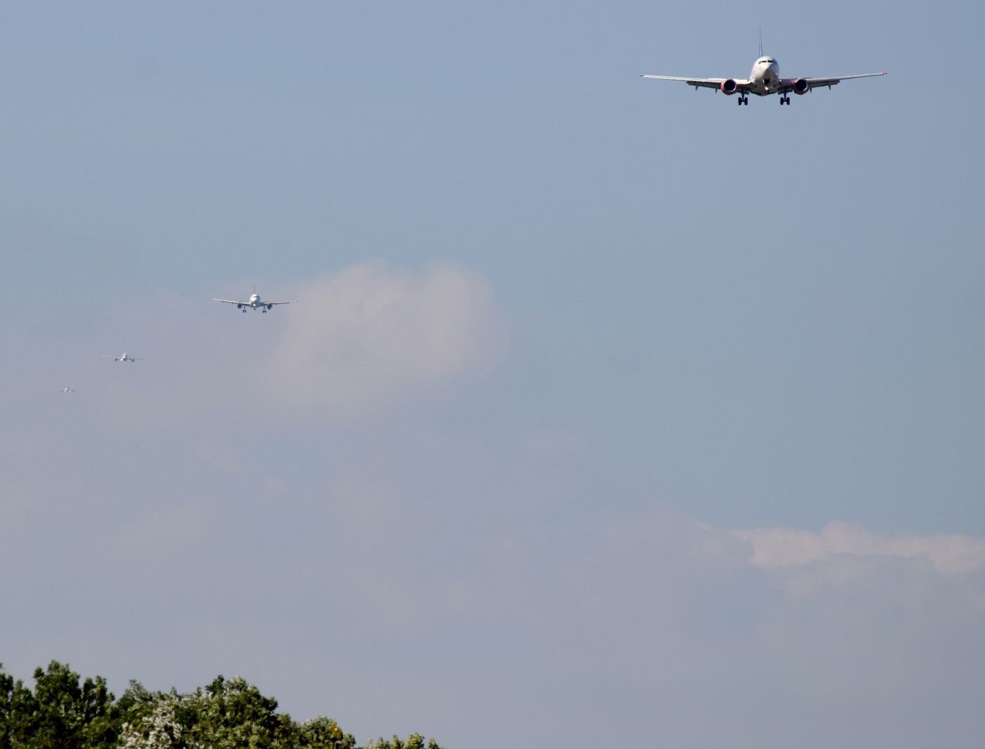 Four airliners strung out in a line across a pale sky on approach to Heathrow, the nearest one high on the right.